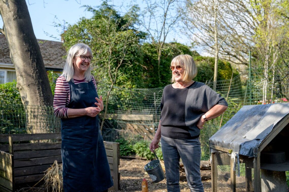 Two elderly women smiling while gardening together outdoors