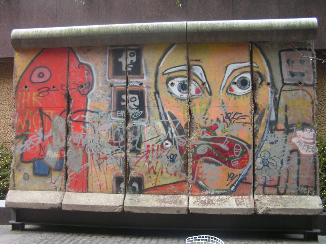 Una lastra di cemento armato del Muro di Berlino, dipinta con figure colorate e stilizzate, esposta su una strada di Manhattan tra i palazzi