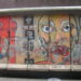 Una lastra di cemento armato del Muro di Berlino, dipinta con figure colorate e stilizzate, esposta su una strada di Manhattan tra i palazzi