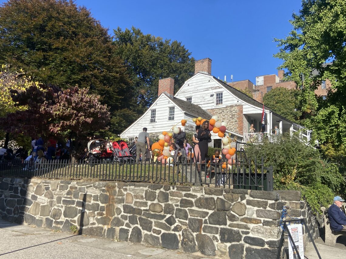 Una casa coloniale olandese in legno a due piani, con veranda e tetto spiovente, in piedi tra il verde in una giornata di sole, a Inwood, New York