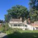 Un piccolo cottage di legno bianco con il portico, circondato da alberi e prati, con i palazzi del Bronx sullo sfondo