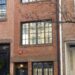 Una casa strettissima in mattoni rossi alta tre piani, con finestre piccole e una porta d'ingresso, incastonata tra altri edifici nel Greenwich Village di New York