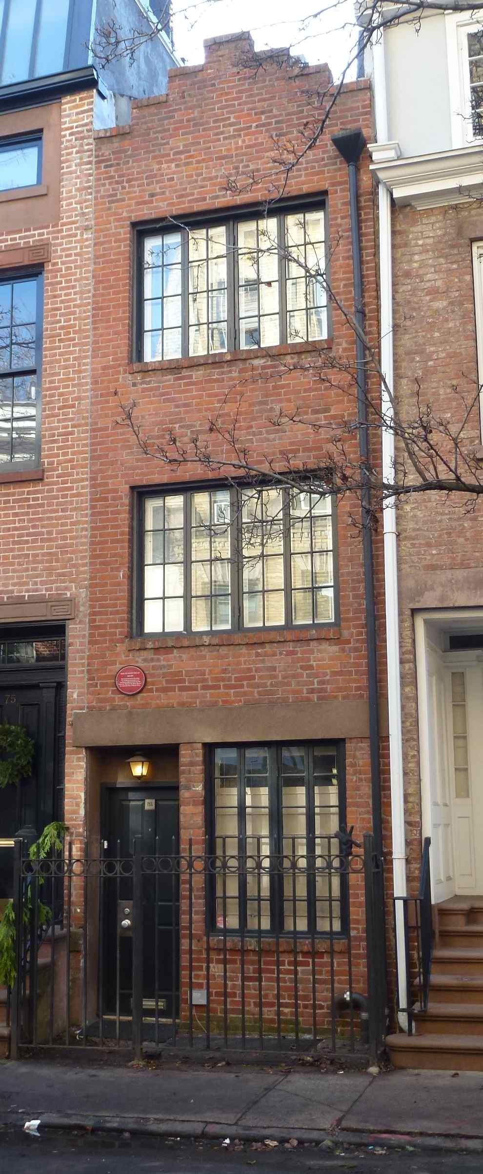 Una casa strettissima in mattoni rossi alta tre piani, con finestre piccole e una porta d'ingresso, incastonata tra altri edifici nel Greenwich Village di New York