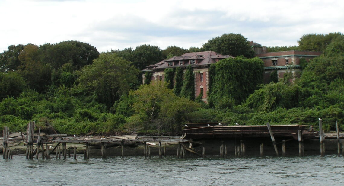 Un edificio in mattoni rossi diroccato e coperto di rampicanti, ai bordi di un prato incolto, sull'isola abbandonata di North Brother, nell'East River di New York