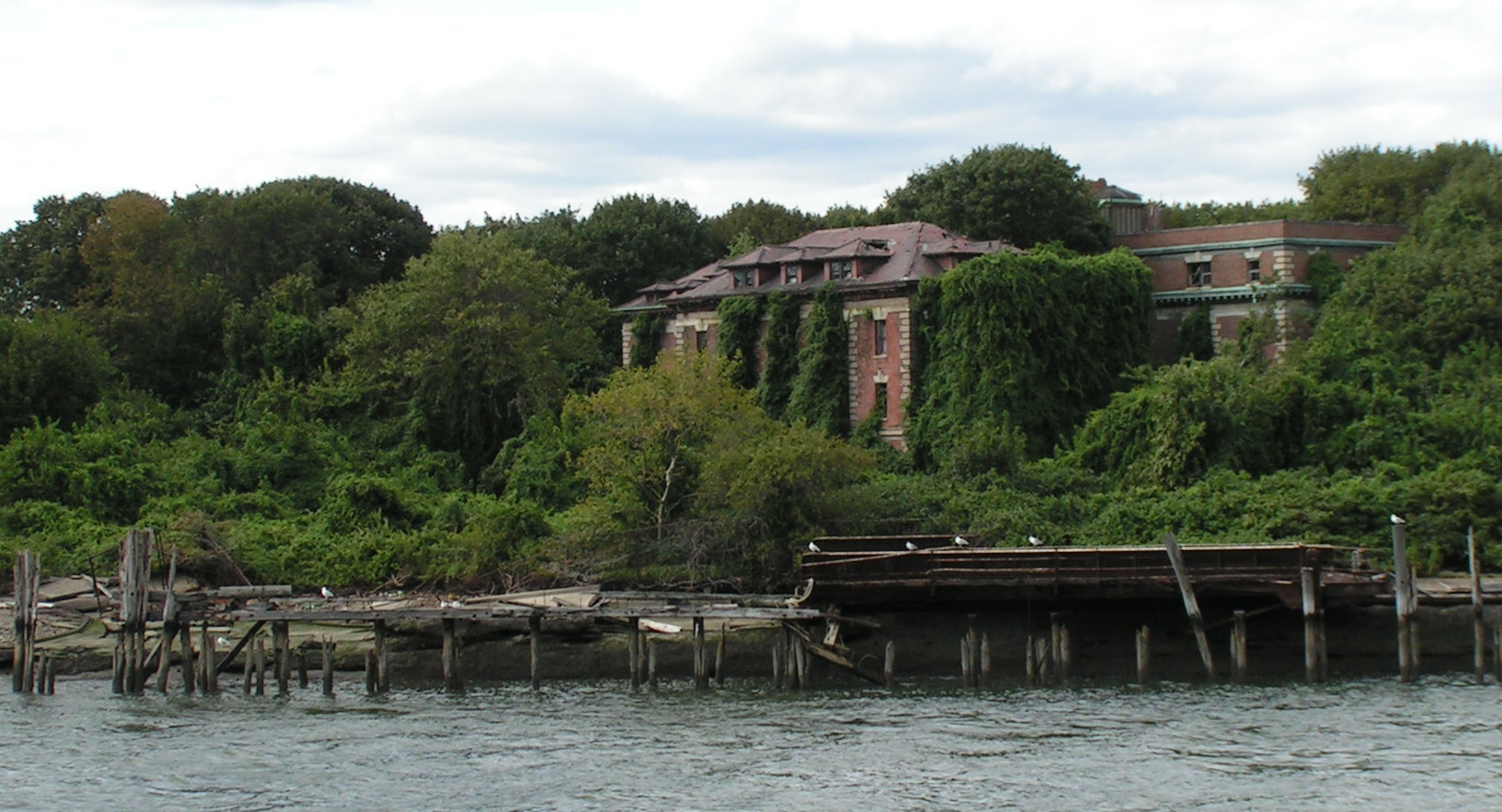 Un edificio in mattoni rossi diroccato e coperto di rampicanti, ai bordi di un prato incolto, sull'isola abbandonata di North Brother, nell'East River di New York