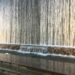 Un piccolo parco urbano lastricato con sedie e tavolini bianchi, alberi che fanno ombra e, sul fondo, una parete attraversata da una cascata d'acqua continua, incastonato tra due palazzi di Manhattan