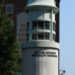 Un piccolo faro conico bianco sormontato da un gabbiotto di vetro e una sfera nera in cima, collocato tra gli edifici del South Street Seaport di New York